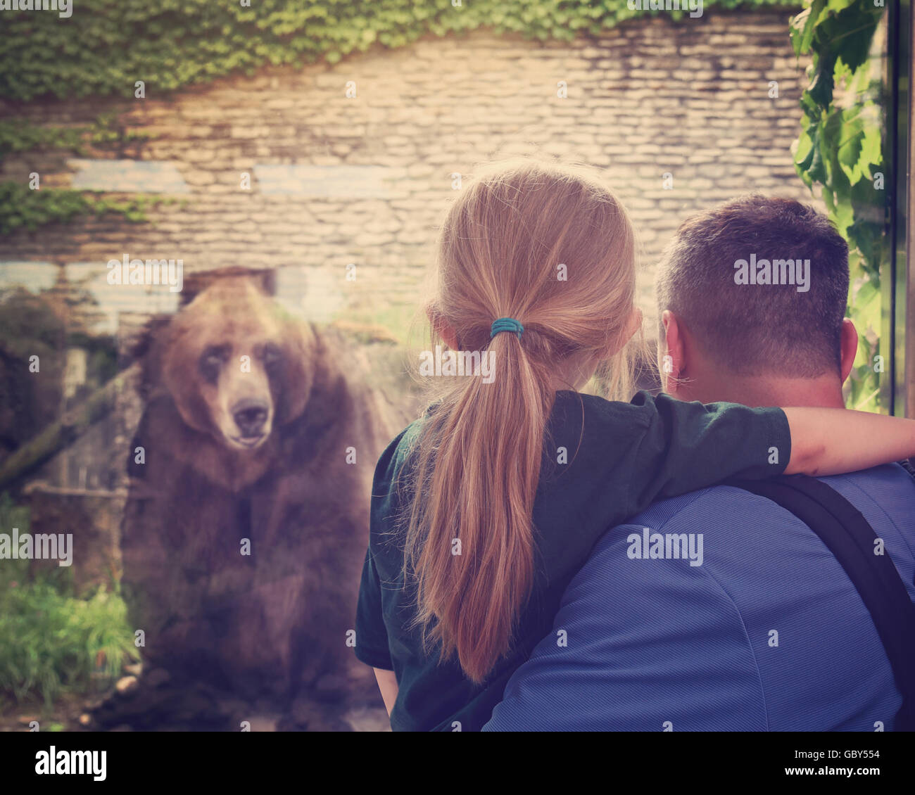 Padre e figlio sono alla ricerca in un vetro allo zoo a un captive orso bruno per una conservazione, estinzione o educazione degli animali Foto Stock