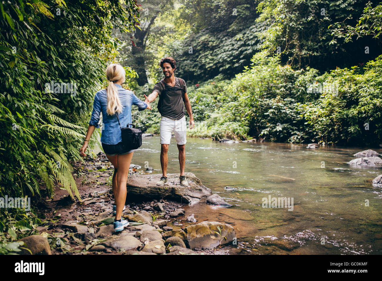 Coppia giovane camminando lungo il torrente di montagna con uomo aiutando la sua ragazza. Giovane su escursionisti in foresta dal flusso. Foto Stock