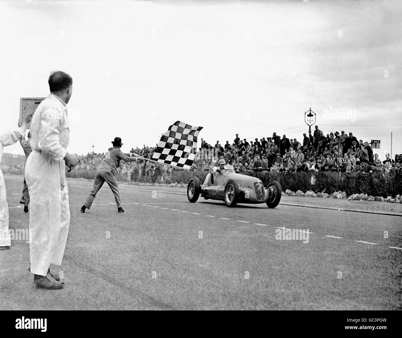 Il pilota britannico Reg Parnell, alla guida di una Maserati 4CL, alza la mano in festa mentre prende la bandiera a scacchi. Foto Stock