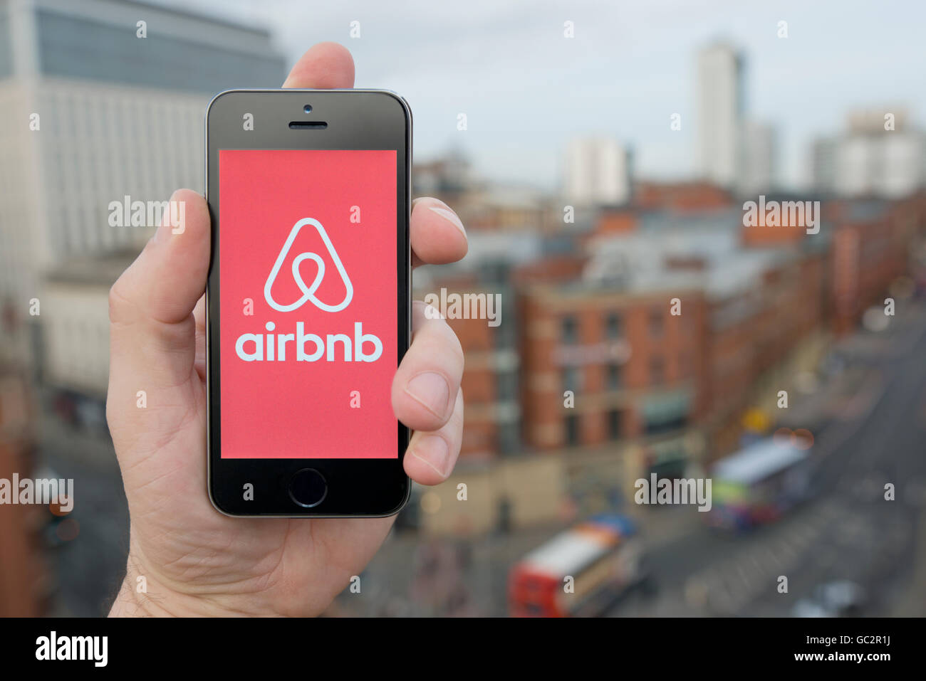 Un uomo utilizza il smartphone Airbnb app mentre si fermò in un alto edificio che si affaccia su una strada trafficata (solo uso editoriale) Foto Stock