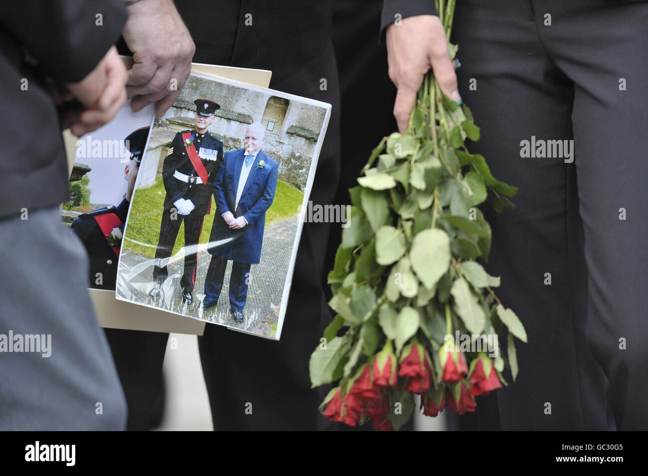 Malcolm Britian, faccia non mostrata ma tenendo le immagini di se stesso al suo matrimonio e del suo migliore uomo Sergente Michael Locket, come il corpo di locket è guidato attraverso Wootton Bassett dopo il suo rimpatrio a RAF Lyneham, Wiltshire. Foto Stock