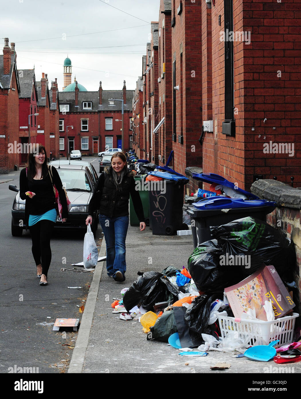 Gli studenti camminano per i mucchi di rifiuti nell'area di Hyde Park di Leeds. I rifiuti sono stati lasciati non raccolti per diverse settimane a causa di un'azione industriale da parte dei raccoglitori di rifiuti. Foto Stock