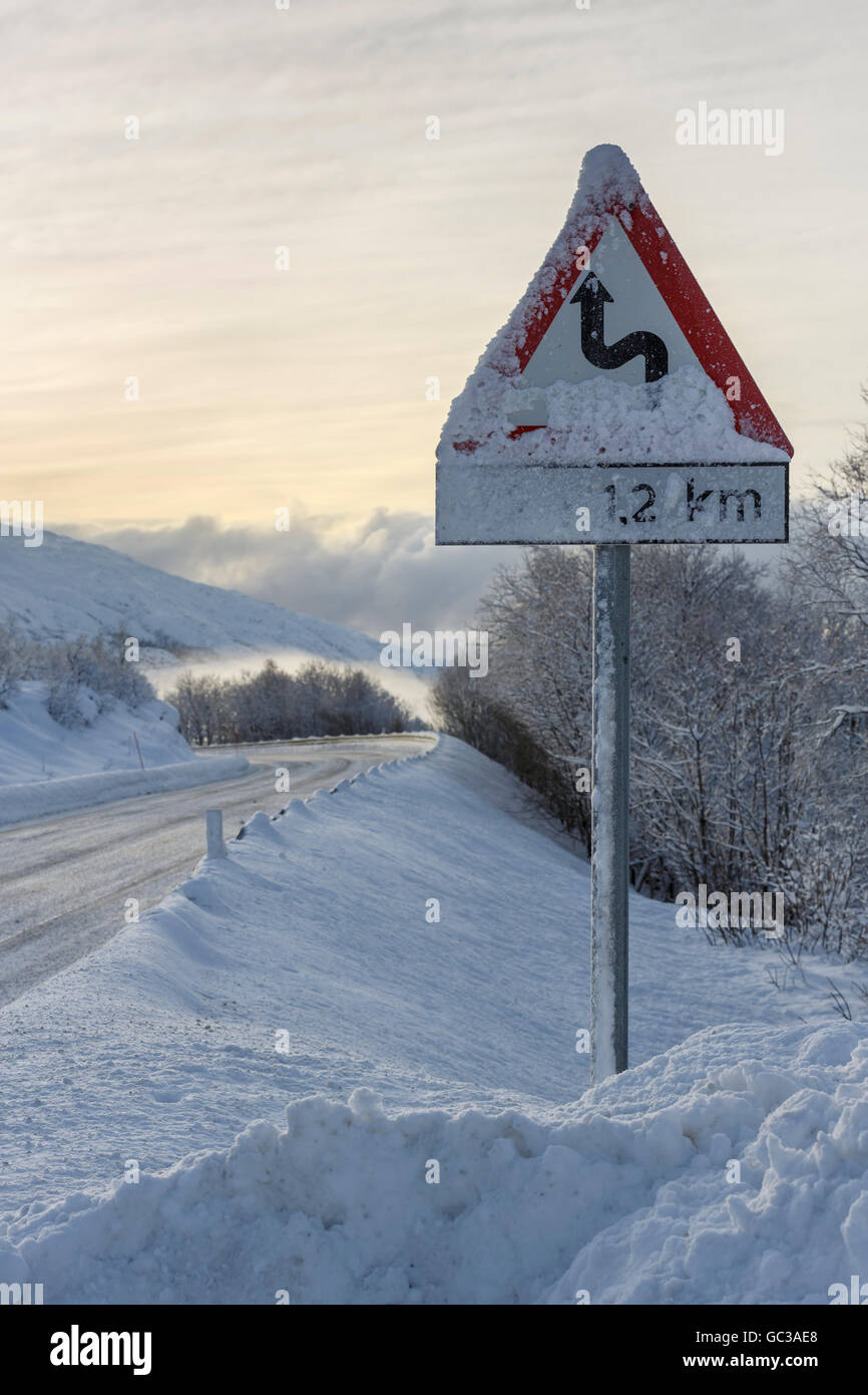 Strada invernale con segnale di avvertimento, percorso europeo E10, avvolgimento percorso, Hinnøya Isola, Nordland, Norvegia Foto Stock