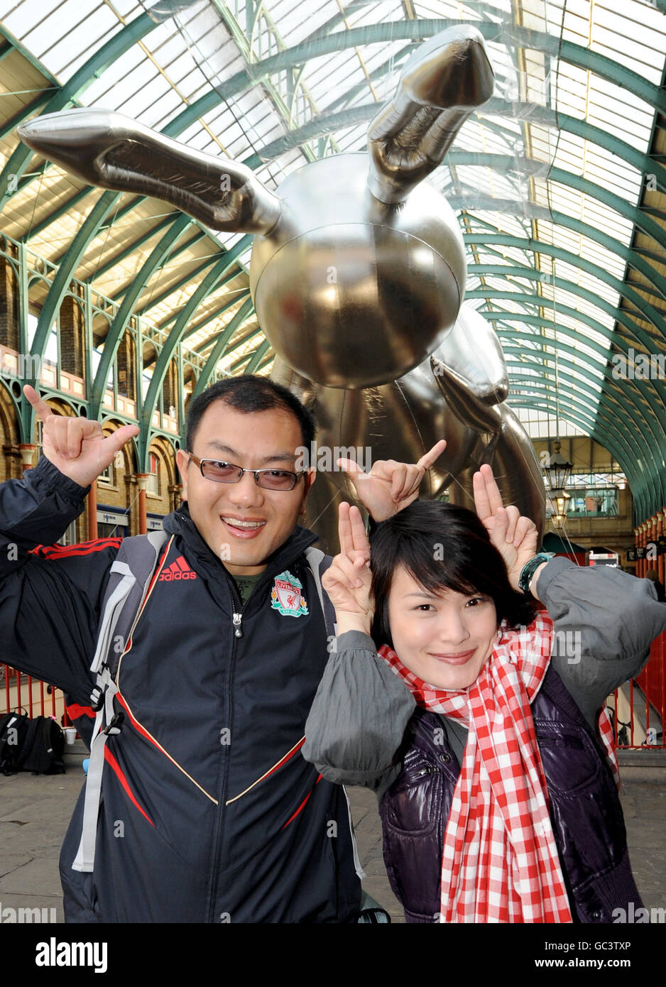 I turisti posano per i fotografi come il gigante palloncino di coniglio dell'artista Jeff Koons 53 piedi è esposto a Covent Garden Market per pubblicizzare Pop Life: Art in a Material World a Tate Modern, Londra. Foto Stock