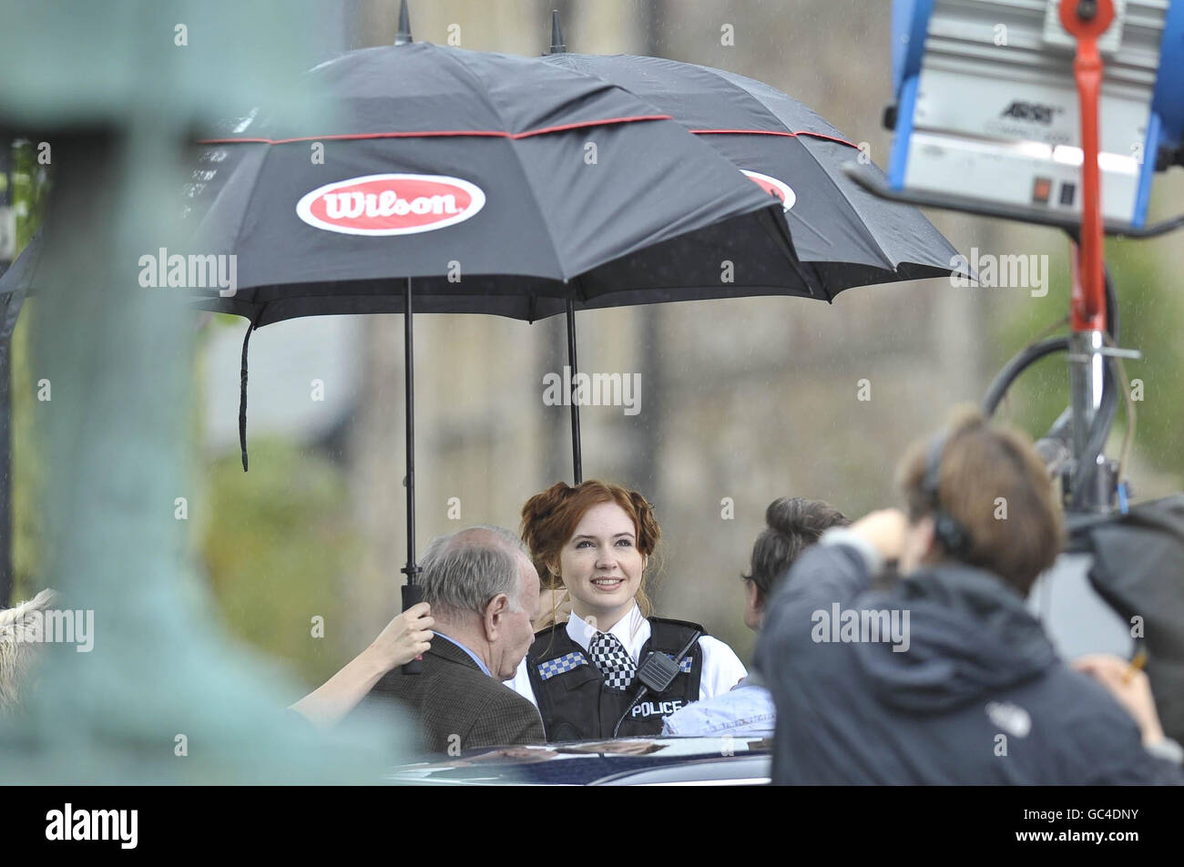 L'assistente del dottore Who, l'attrice Karen Gillan, vestita come ufficiale di polizia, è schermata dalla pioggia durante le riprese sul set vicino alla cattedrale di Llandaff, Cardiff, Galles, dove è stata girata l'ultima serie di Doctor Who. Foto Stock