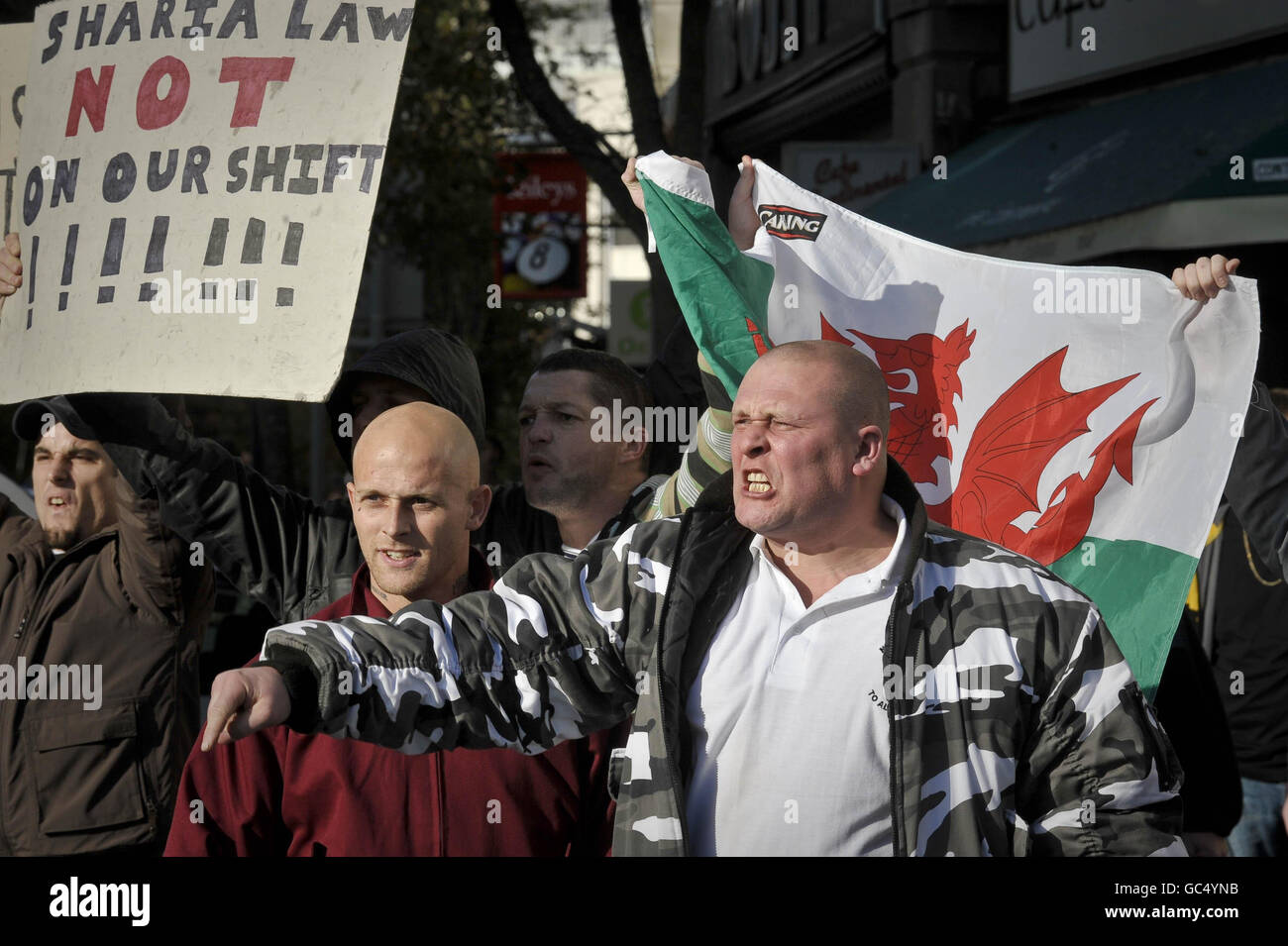 I manifestanti della Welsh Defense League cantano indietro contro i manifestanti antifascisti mentre i due gruppi sono tenuti separati dalla polizia durante una protesta vicino a Castle Square, Swansea, Galles. Foto Stock