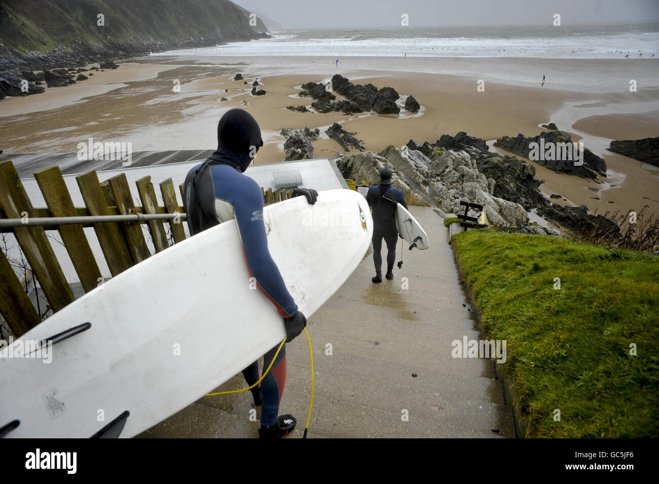 I surfisti si dirigano verso il mare in mute, stivali, guanti e berretti a Putsborough, North Devon, dove forti venti hanno causato grandi ondate. Foto Stock