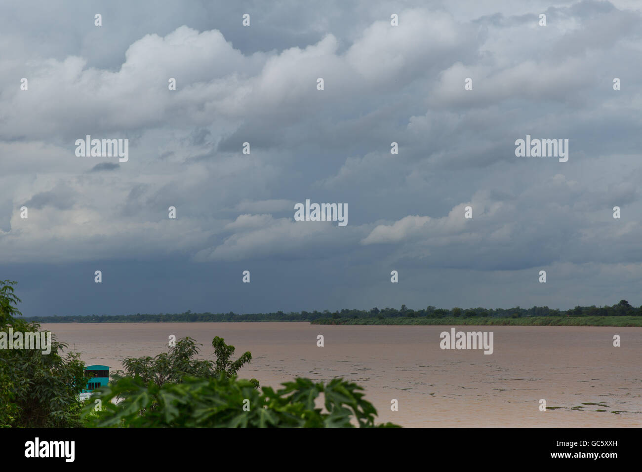 Terreni fangosi del fiume Mekong tra Thailandia e Laos in un giorno nuvoloso durante la stagione delle piogge, acquazzone nel lontano sullo sfondo Foto Stock