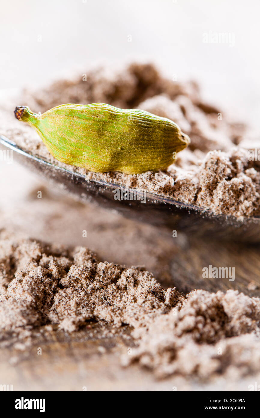 Baccello di cardamomo giacente sul cucchiaio di spezie in polvere. Foto Stock