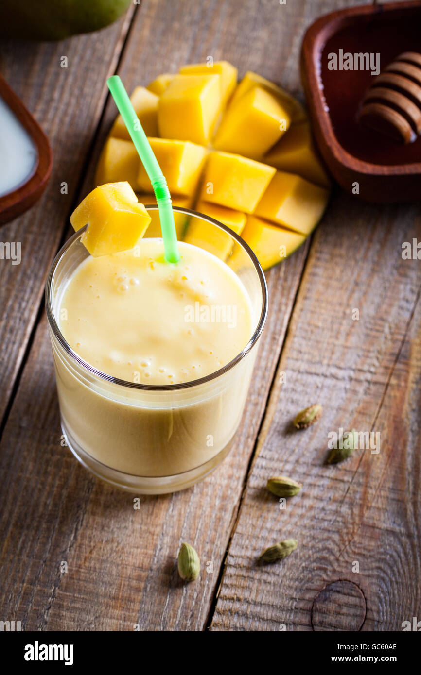 Bicchiere di mango lassi Indian bevanda aromatizzata con il cardamomo. Frullato su sfondo di legno. Foto Stock