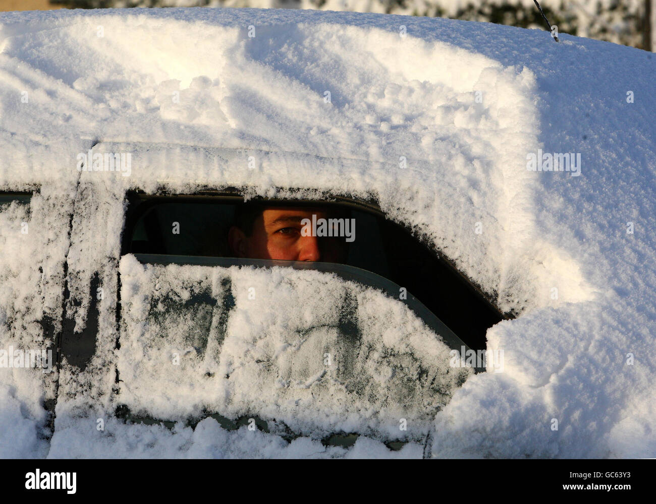 Un uomo guarda fuori dalla sua finestra dopo aver eliminato la neve dalla sua auto a St Boswells, nei confini scozzesi, dopo una notte di nevicate pesanti. Foto Stock
