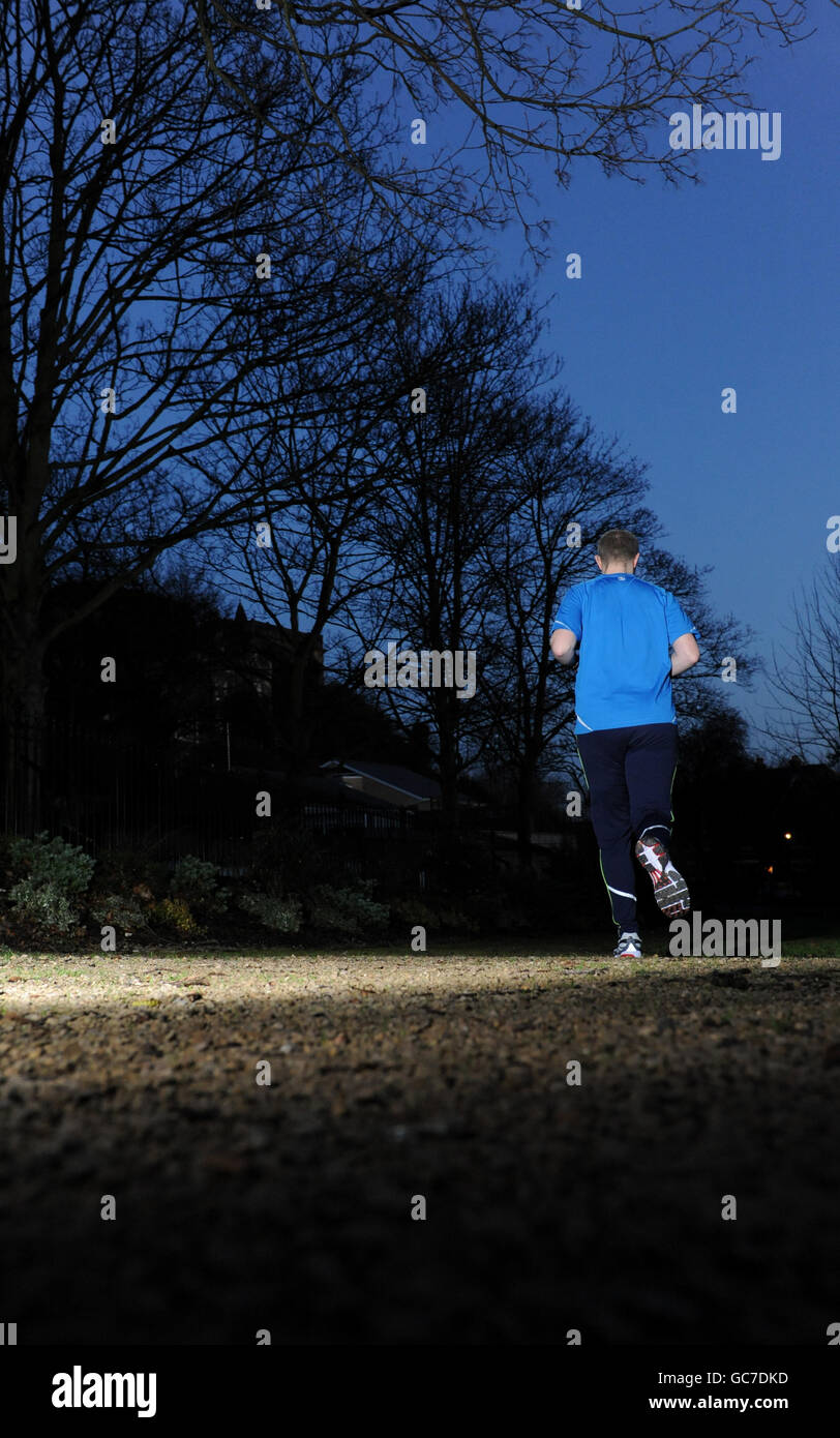 Stock generale, Sport e Fitness. Uno jogger si fa strada attraverso un parco al tramonto Foto Stock