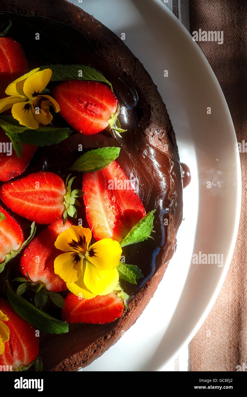 Torta al cioccolato con fragole e eddible fiori in un estate paglierino Foto Stock