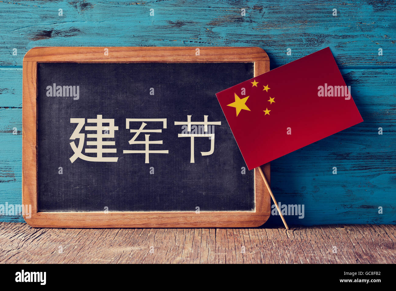Una lavagna con l'esercito di testo giorno scritto in cinese e la bandiera della Cina su un rustico di una superficie di legno, contro una in legno di colore blu Foto Stock