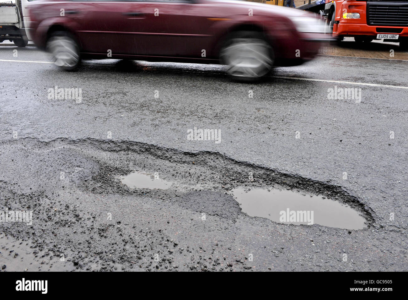 Un'auto guida oltre un pothole su Broomhill Road, Bristol. Foto Stock