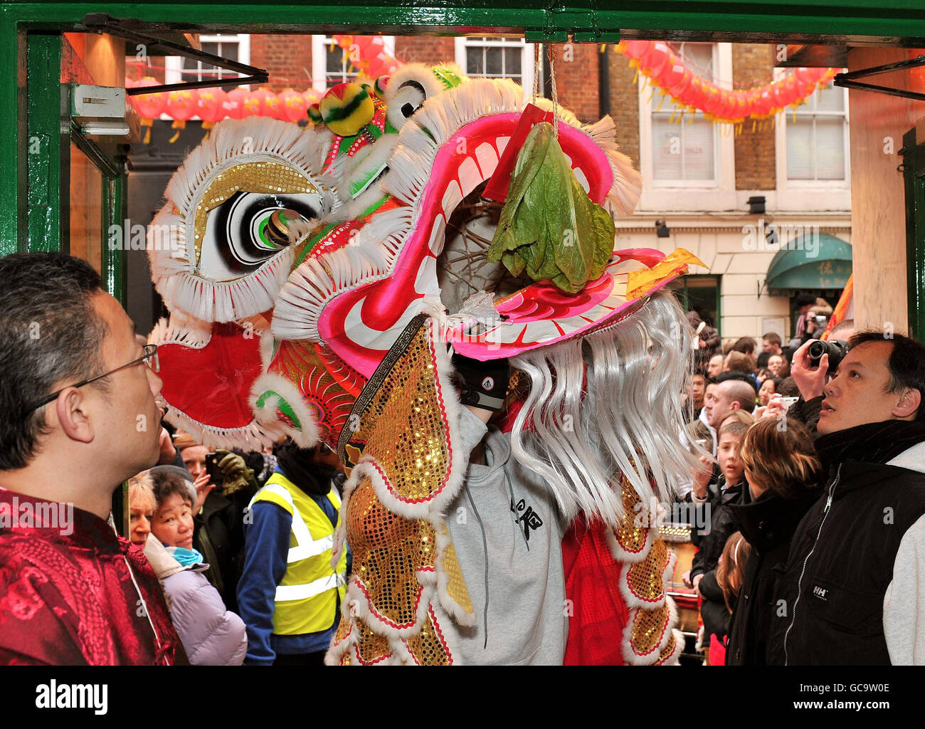 La gente celebra l'inizio dei festeggiamenti per il nuovo anno cinese mentre un leone cinese tradizionale si fa strada attraverso le strade affollate di Chinatown, Londra. Foto Stock