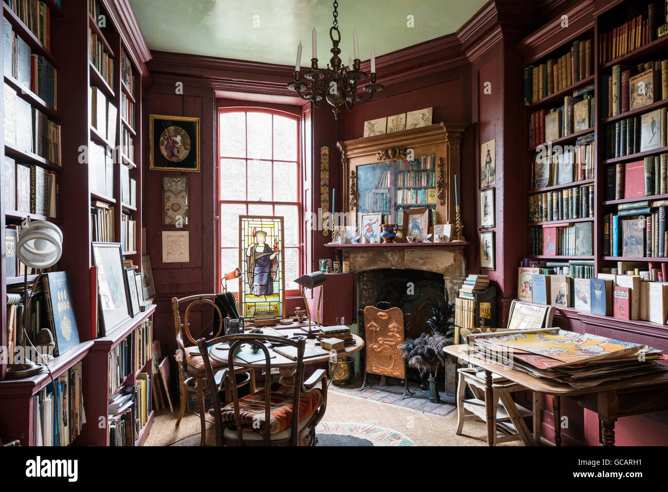 Rosso con pannelli in legno quirky biblioteca con caminetto in stile georgiano e un assortimento di opere d'arte Foto Stock