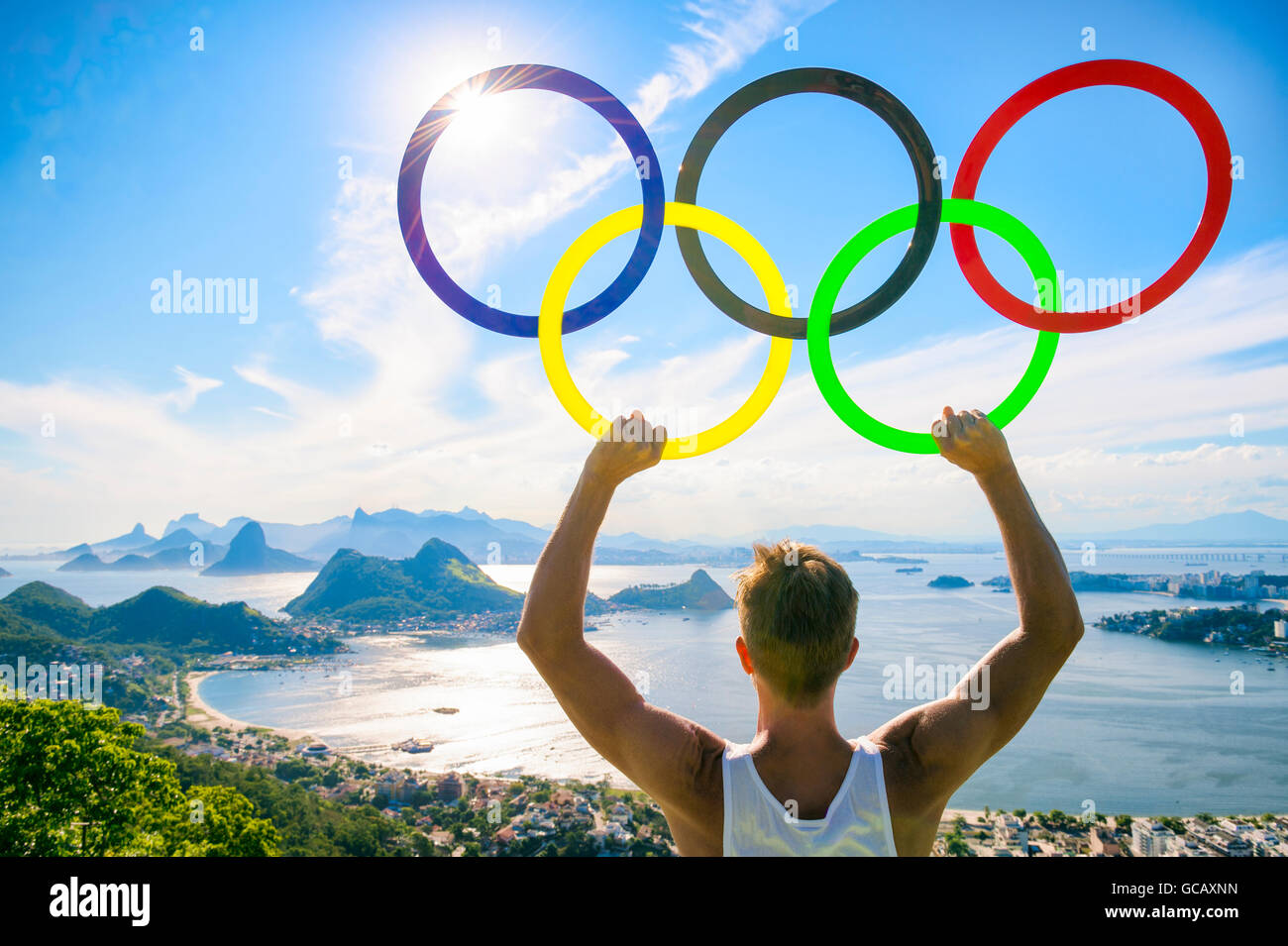 RIO DE JANEIRO - MARZO 21, 2016: un atleta detiene anelli olimpici sotto il luminoso cielo blu al di sopra dello skyline della citta'. Foto Stock