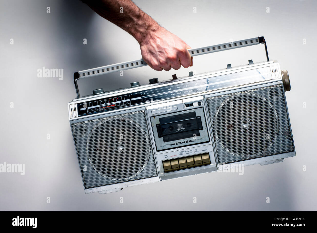 Una mano d'uomo in possesso di un vecchio stereo con riproduttore di cassette contro un muro bianco; Regina, Saskatchewan, Canada Foto Stock