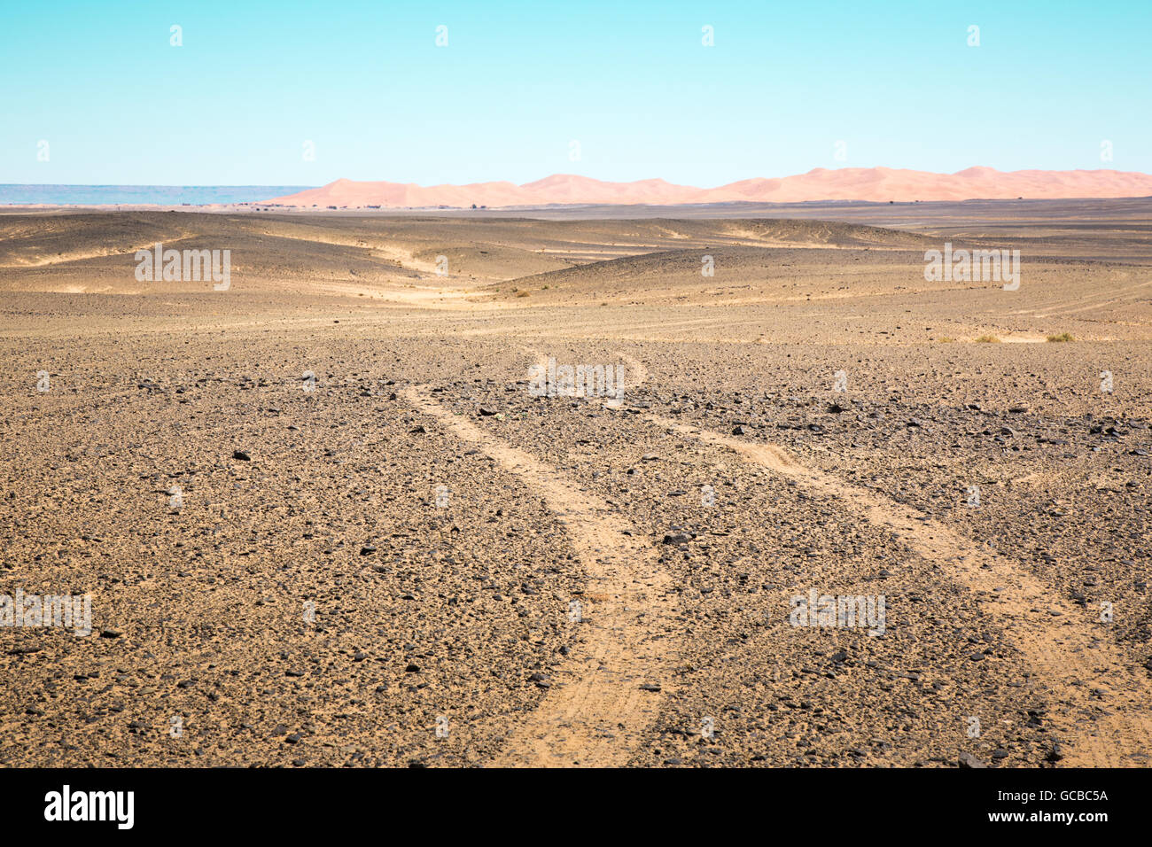 Le tracce del veicolo in Marocco deserto, allontanandosi dalla videocamera verso le montagne e il mare in lontananza. Foto Stock