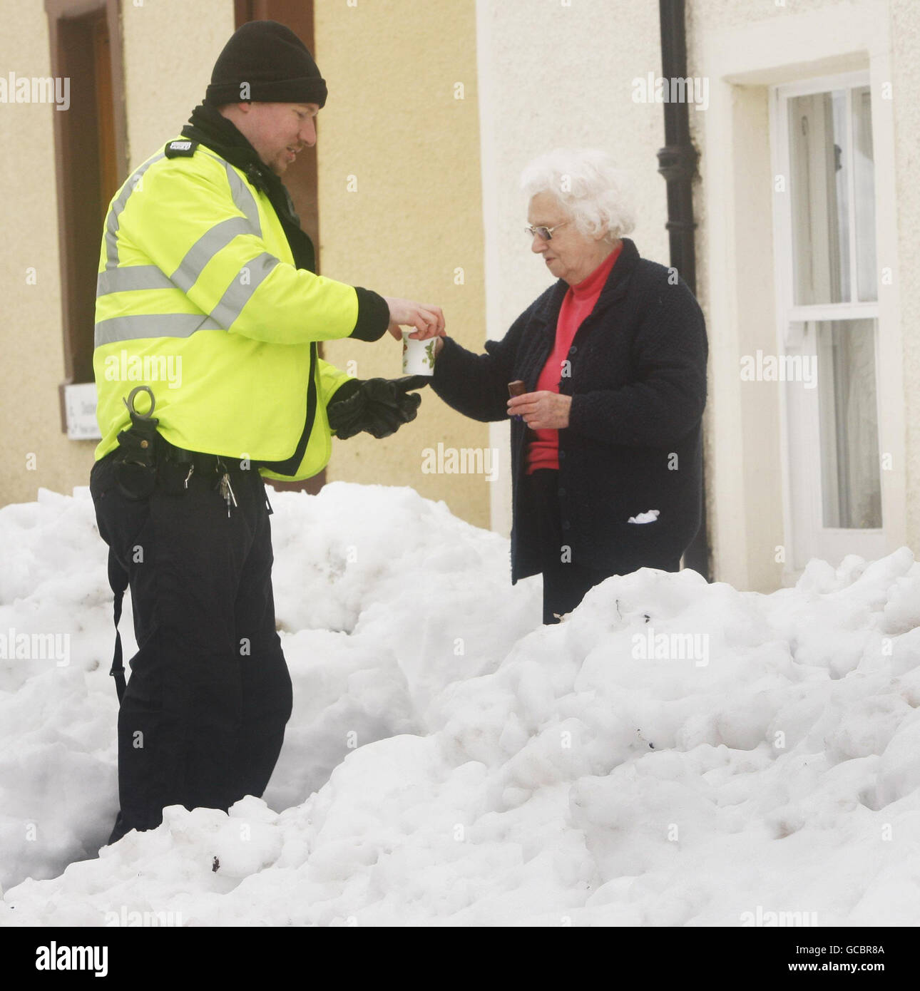 Un residente locale porta una tazza di tè a un uomo di polizia in condizioni di neve ad Auchterarder, Scozia, mentre il freddo scatto continua. Foto Stock