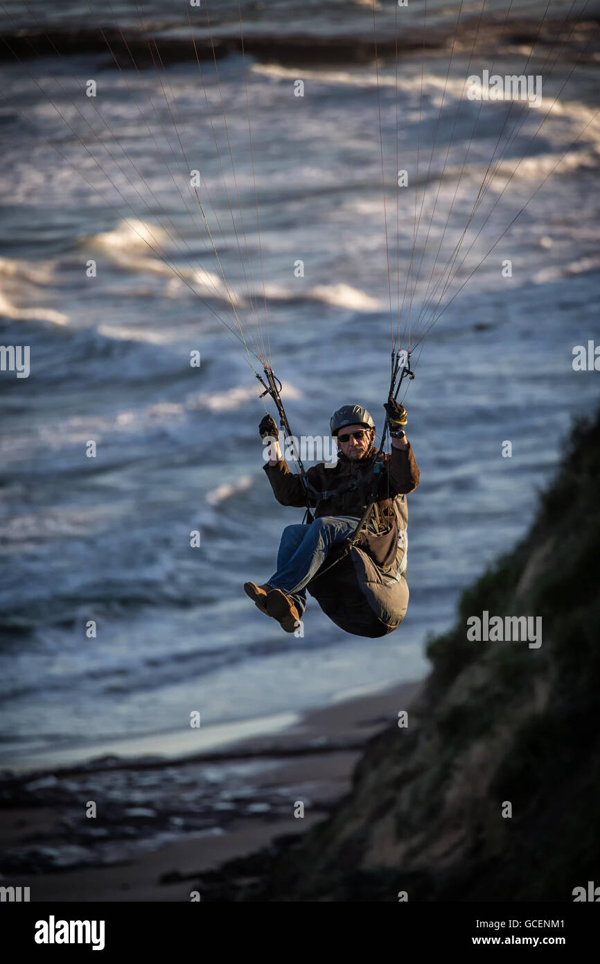 Un uomo vola il suo parapendio lungo la clifftops. Il deltaplano è famoso anche qui a Sydney le spiagge del nord della penisola. Foto Stock