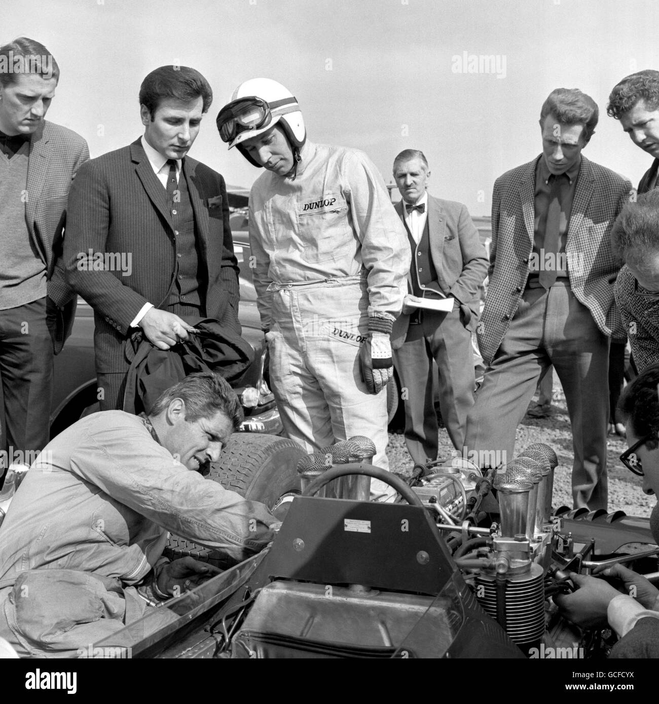 Il pilota campione del mondo John Surtees guarda un rapido cambio di spina effettuato sulla sua Ferrari prima dello start della prima parte delle due parti Race of Champions per le vetture internazionali di Formula 1 sul circuito Brands Hatch, vicino a Swanley. I Surtees hanno concluso sesto in questa parte della gara. Foto Stock