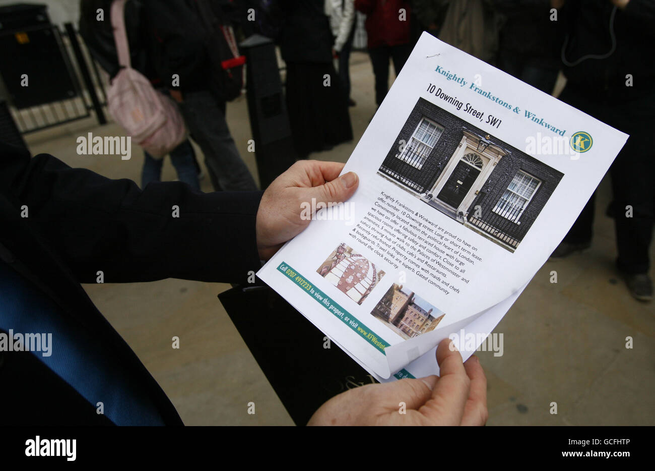 Un uomo che si pone come un incrocio tra un agente immobiliare e il leader del Partito conservatore David Cameron detiene un prospetto di agente immobiliare di 10 Downing Street, durante un'astuzia politica fuori Downing Street a Westminster, nel centro di Londra, con l'avvicinarsi del giorno delle elezioni generali. Foto Stock