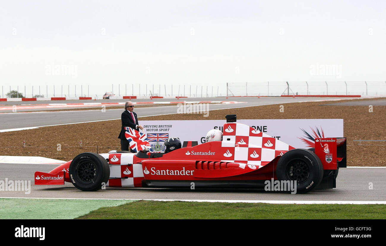 Sir Jackie Stewart ondeggia la bandiera dell'Unione per inviare il Duca di York e il Presidente della BRDC Damon Hill in un giro di apertura in una vettura da corsa a due posti del nuovo circuito di Silverstone. Foto Stock