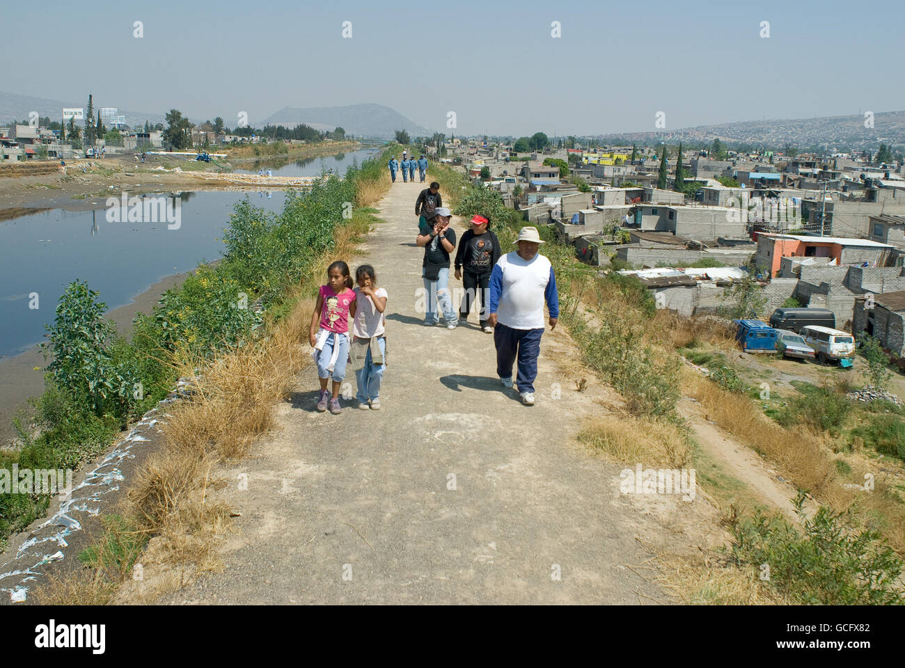 Residenti a piedi lungo un argine di terracotta, costruito per contenere le acque luride e le acque di pioggia della La Compania canal in Valle de Chalco. Foto Stock