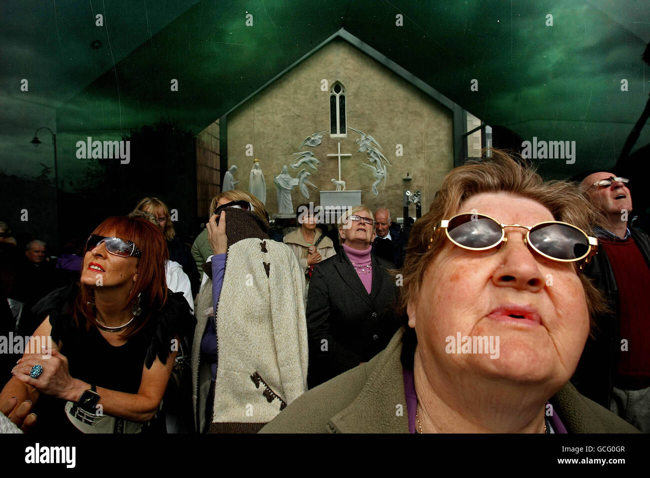 Le persone indossano occhiali da sole per proteggere i loro occhi dal sole  mentre Joe Coleman 'visionario' di Dublino prega a Knock Shrine Co Mayo  dove afferma di essere testimone di una