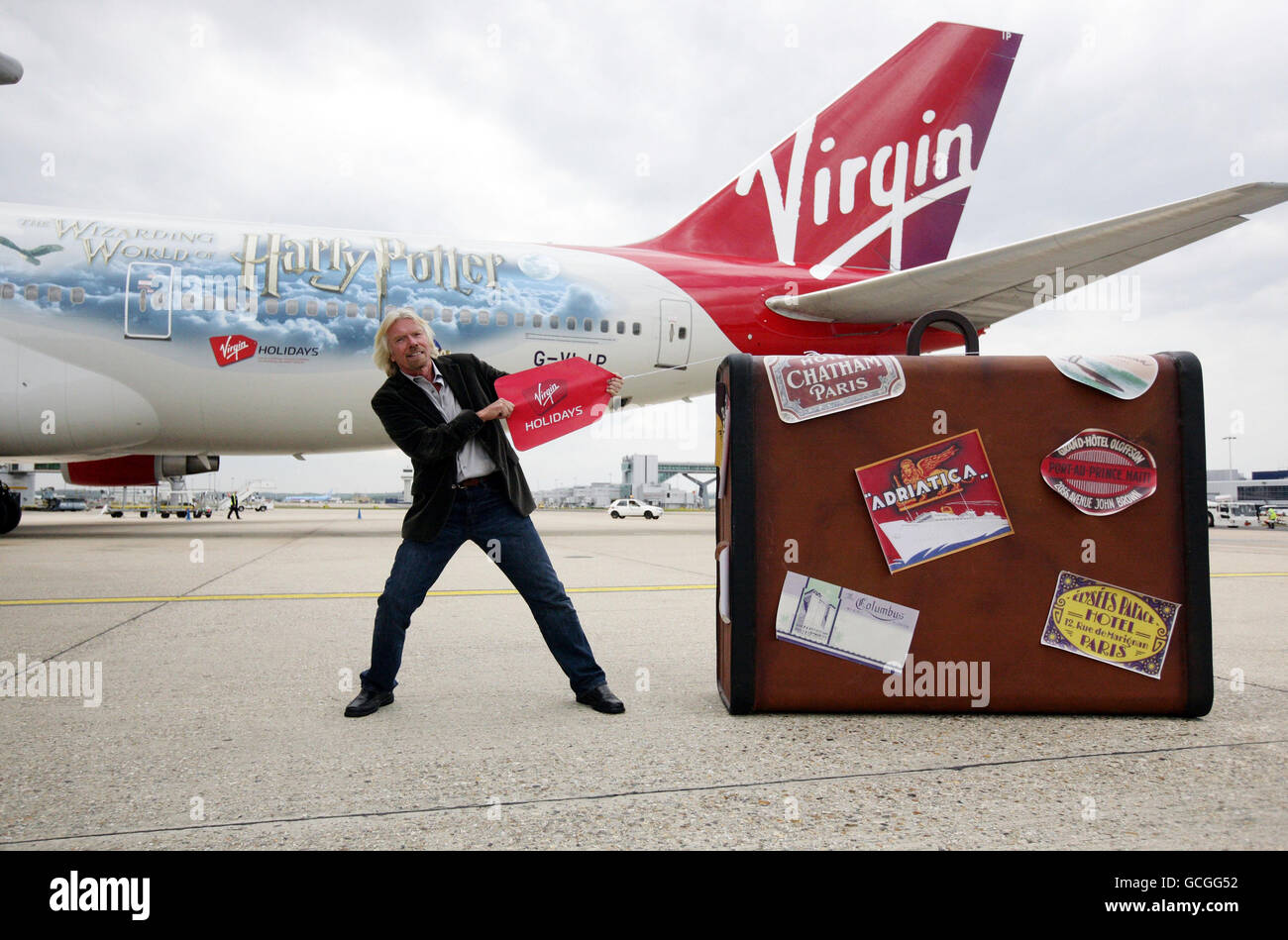 Sir Richard Branson tira una valigia gigante all'aeroporto di Gatwick,  Sussex, di fronte ad un velivolo virgin con la livrea di Harry Potter  durante una chiamata fotografica per celebrare il 25° anniversario