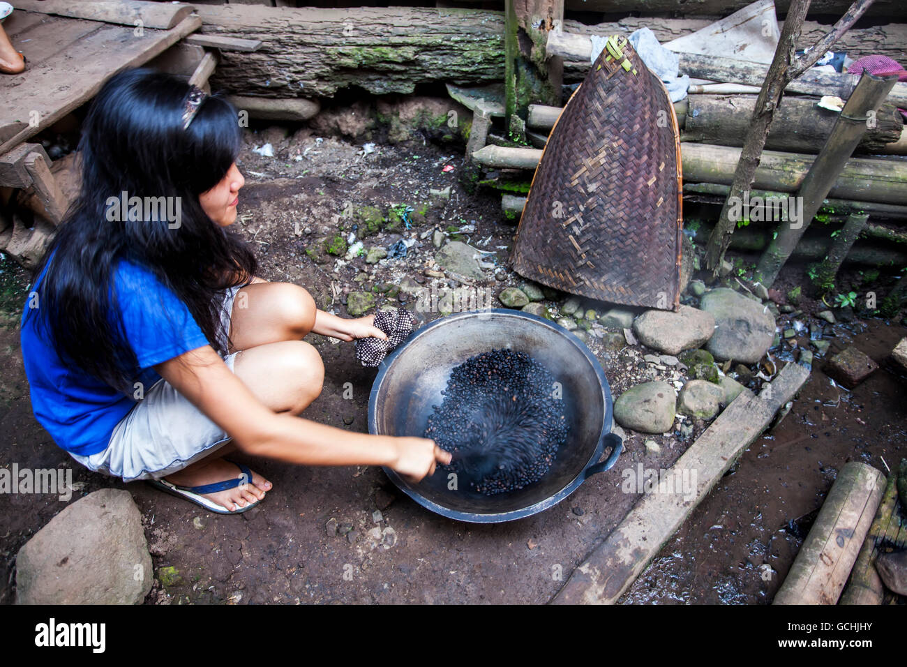 Un giovane residente Lintang arrosti i chicchi di caffè nel suo cortile in un wok; Sumatra, Indonesia Foto Stock