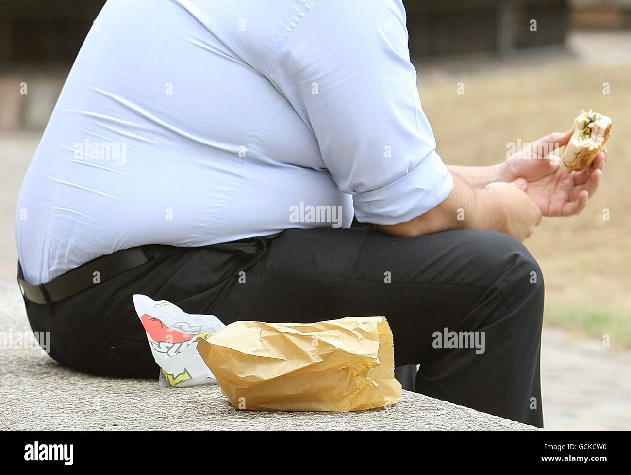 Un uomo in sovrappeso mangia cibo veloce. Il GPS e altri professionisti della salute dovrebbero dire alle persone che sono grassi piuttosto che obesi, ha detto oggi un ministro della salute. Foto Stock