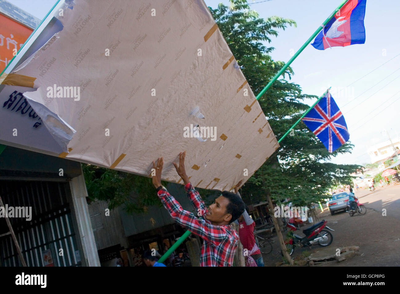 Un uomo è il sollevamento di un segno che indica la posizione di una nuova scuola di lingua inglese nel villaggio di Chork, Cambogia. Foto Stock