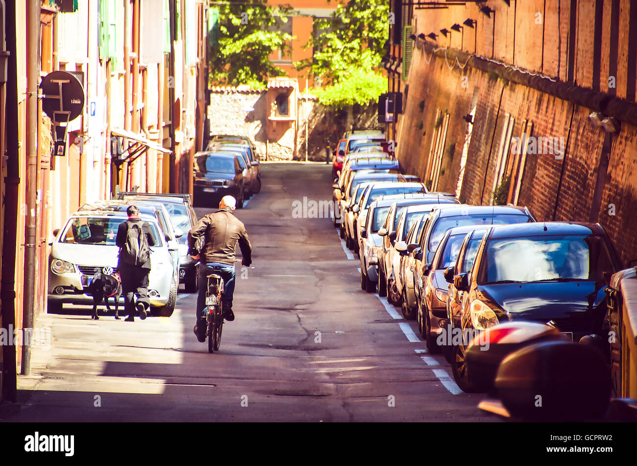 Bologna, Italia uomo calvo cross street con la bicicletta a fianco di una fila di automobili parcheggiate Foto Stock