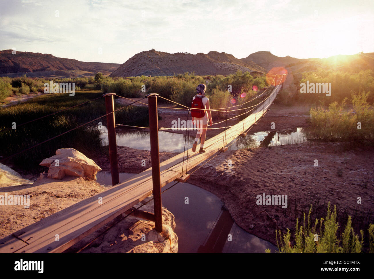 Escursionista femmina attraversando ponte pedonale al tramonto; Southern Utah deserto; USA Foto Stock