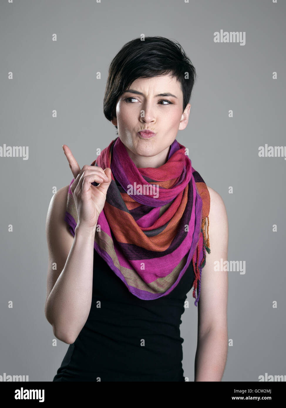 Bellezza arrabbiato con colorati scialle scolding dito guardando lontano oltre il grigio di sfondo per studio. Foto Stock