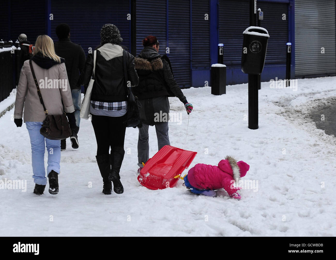 Anche andare a scuola con una slitta era pericoloso nel centro di Newcastle, perché un bambino prende un tumble mentre viene tirato su una slitta da un adulto, dopo un'altra notte di nevicate pesanti. Foto Stock