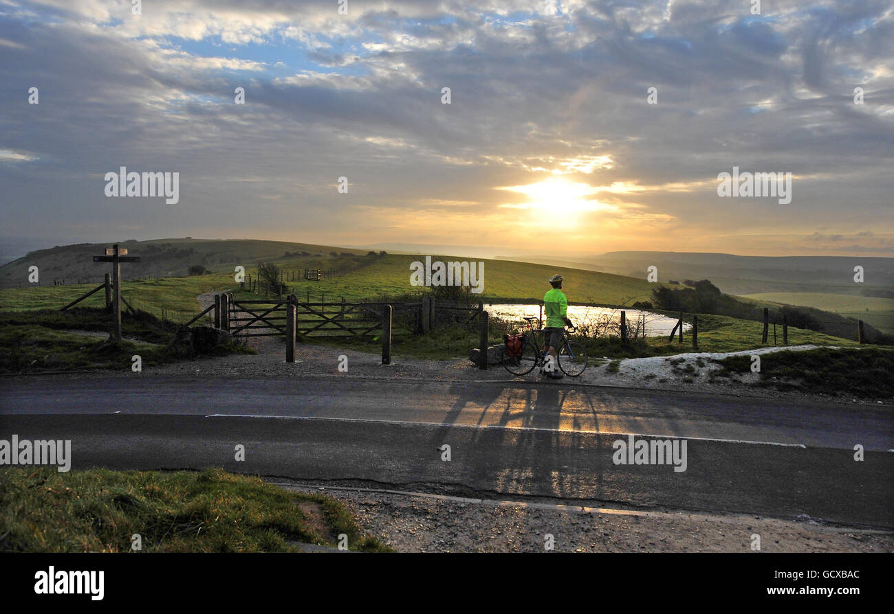 Un ciclista si ferma per ammirare l'alba questa mattina in cima al Ditchling Beacon, vicino a Brighton. Foto Stock