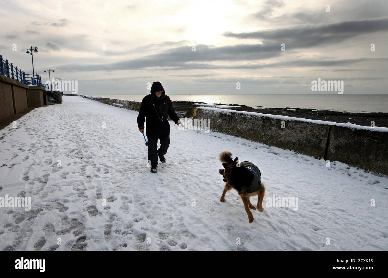 Collin Woods e il suo cane Zeb fare una passeggiata innevata sul lungomare di Porthcawl, Galles meridionale. Foto Stock