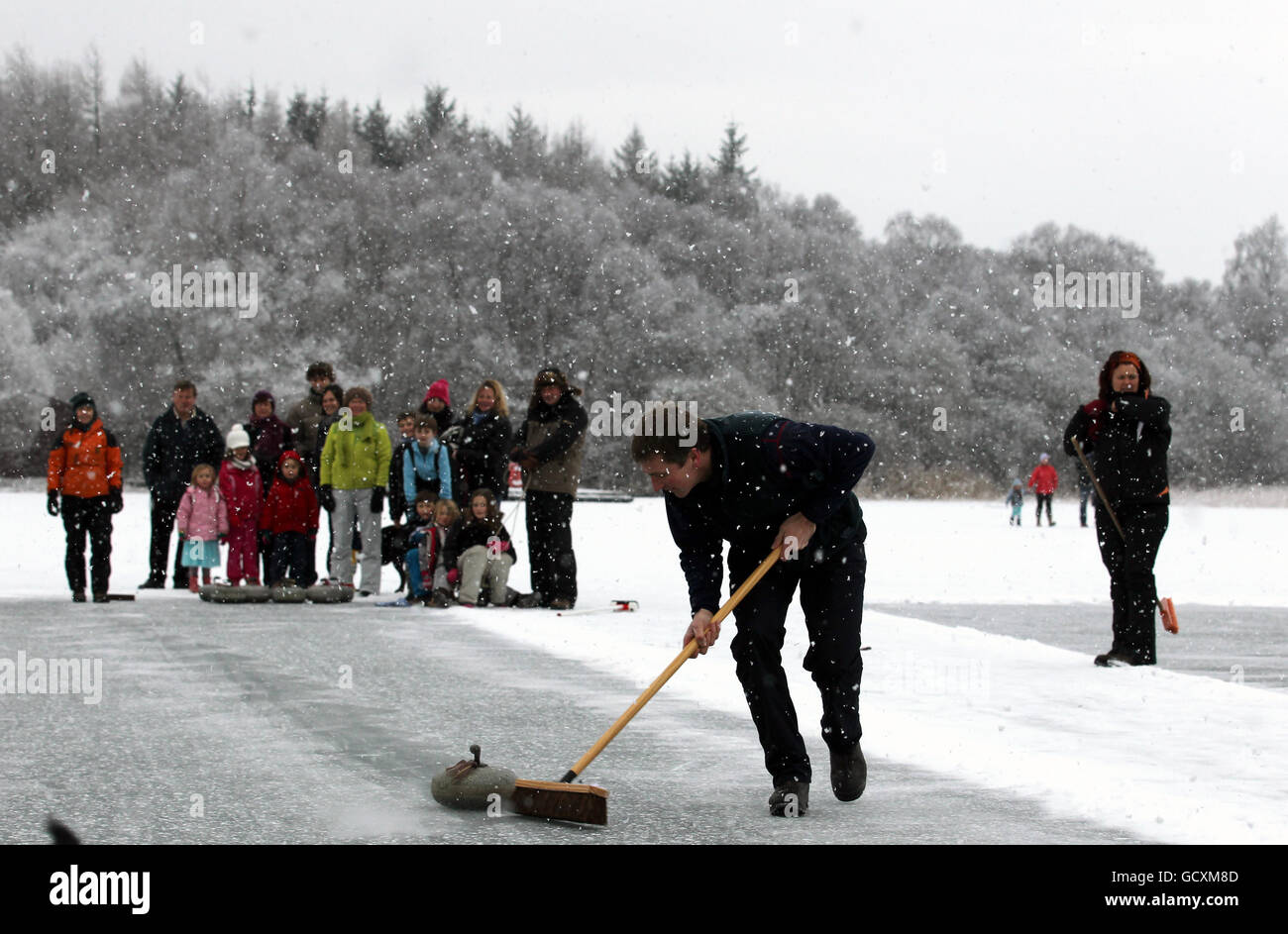 Nigel Holl spazza una pietra durante la partita di curling della Stanley Cup tra il club di curling Blair Drummond e il Port of Menteith Curling Club che si tiene su un lago ghiacciato di Menteith. Foto Stock