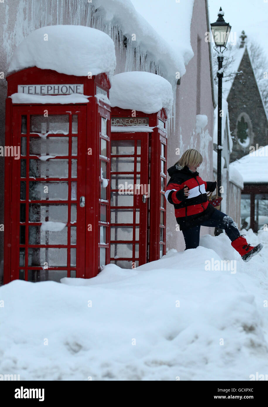 Una donna lascia una scatola telefonica coperta di neve a Braemar, mentre la neve continua a coprire gran parte del Regno Unito. Foto Stock