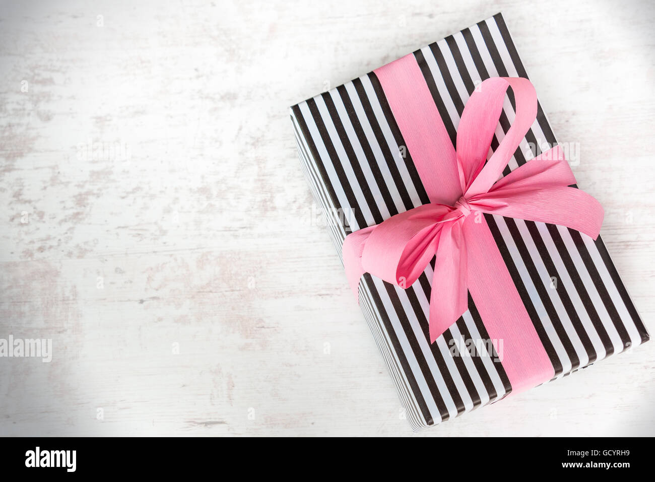 Confezione regalo avvolto in bianco e nero a strisce di carta con nastro rosa su di un legno bianco sfondo vecchio Foto Stock