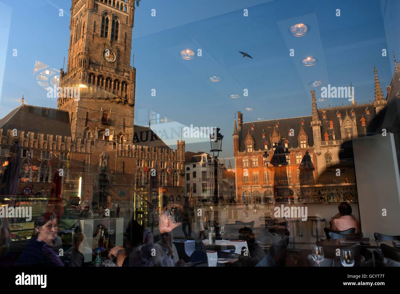 La riflessione in un ristorante di vetro del Grote Markt nel crepuscolo della sera e Belfort van Brugge Foto Stock