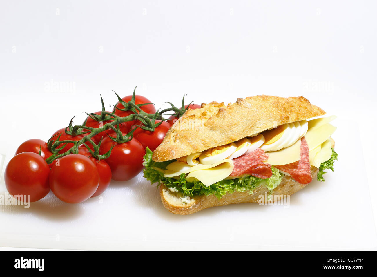 Baguette bun e rabboccato con salame, formaggio, lattuga e uova sode su un bianco tagliere in plastica Foto Stock