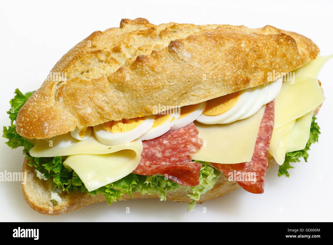 Baguette bun e rabboccato con salame, formaggio, lattuga e uova sode su un bianco tagliere in plastica Foto Stock
