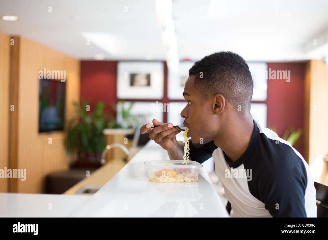 Closeup ritratto giovane uomo bello mangiare tagliatelle, seduti al tavolo bianco guardare qualcosa, isolato, lussuosi interni urbani Foto Stock