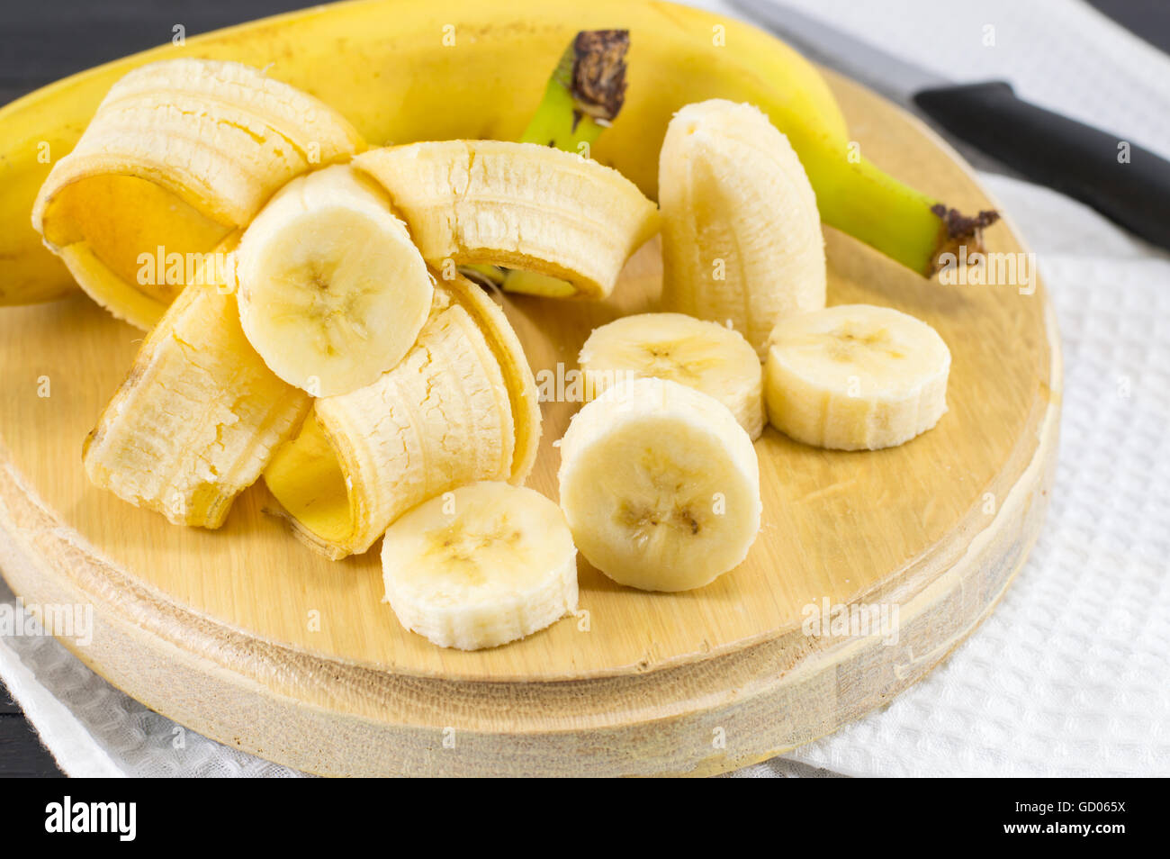 Le banane fresche tagliate a fette su bianco tessile e vassoio in legno Foto Stock