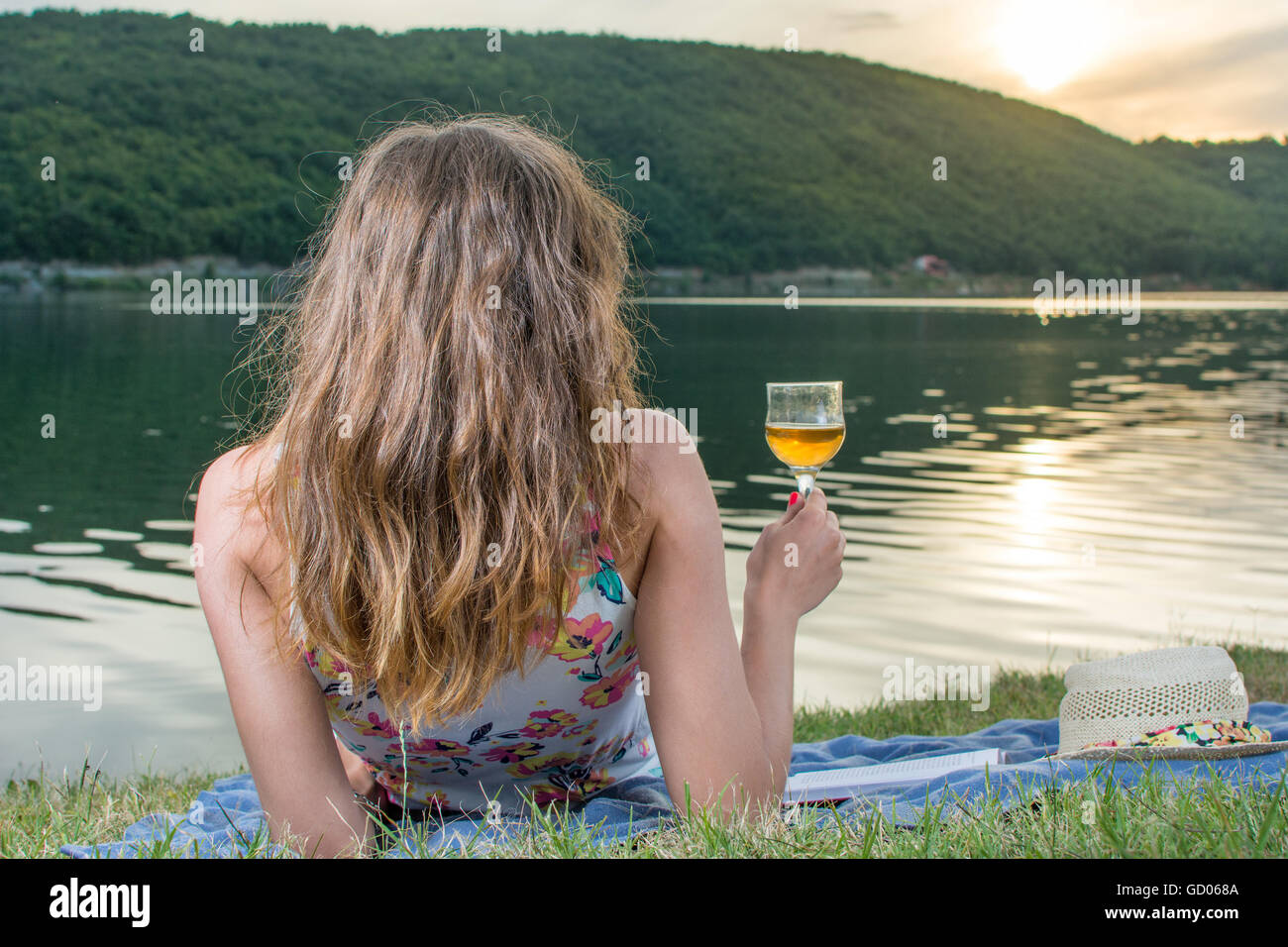 Donna con un bicchiere di vino in riva al lago Foto Stock